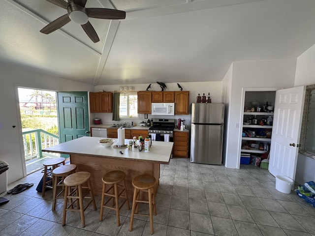 kitchen featuring ceiling fan, a center island, stainless steel appliances, lofted ceiling, and a kitchen bar