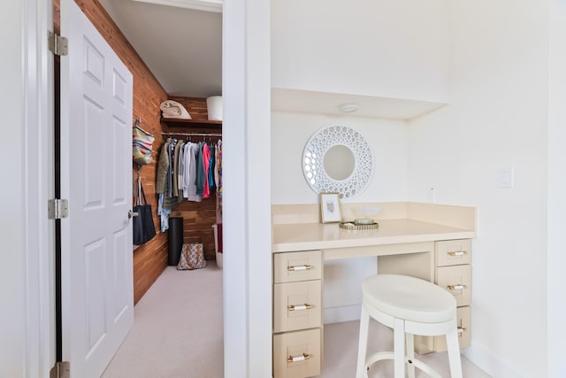 home office featuring light carpet, built in desk, and wood walls