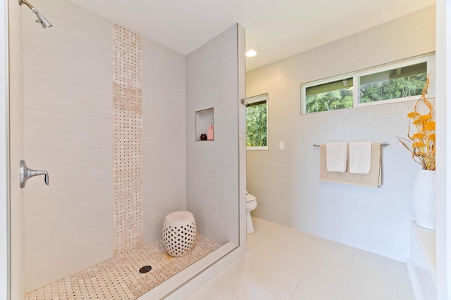 bathroom with toilet, tile patterned flooring, tile walls, and walk in shower