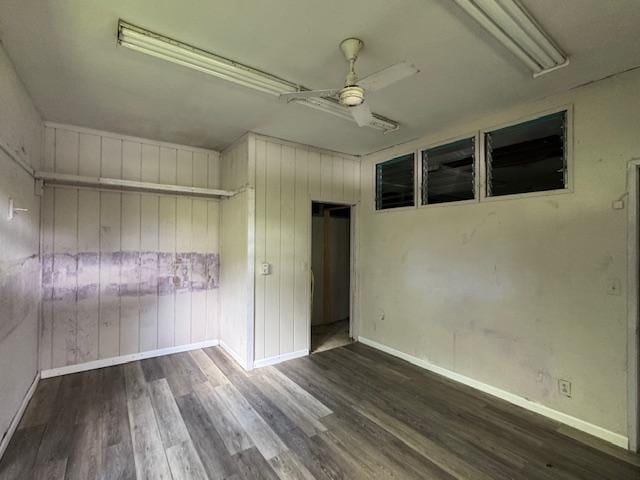 unfurnished room featuring ceiling fan, dark wood-type flooring, and wood walls