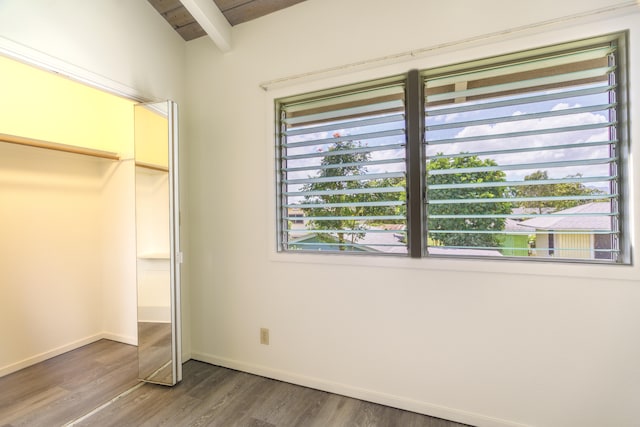 unfurnished bedroom with beamed ceiling, baseboards, a closet, and wood finished floors