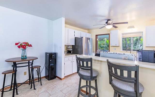 kitchen featuring a kitchen breakfast bar, kitchen peninsula, stainless steel fridge, and white cabinets