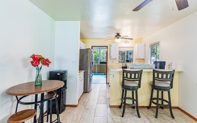 kitchen with a breakfast bar, stainless steel fridge, light tile patterned floors, and white cabinetry