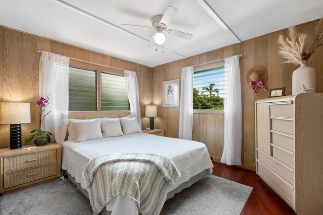 bedroom with ceiling fan, wooden walls, and wood finished floors