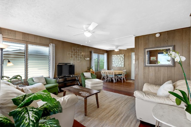 living area featuring wood walls, ceiling fan, a textured ceiling, and wood finished floors