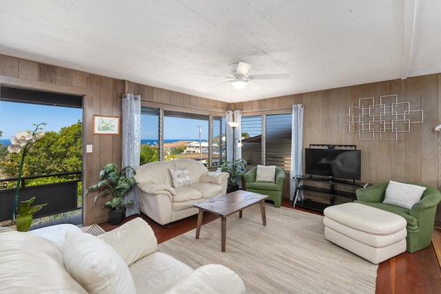 living area with ceiling fan, wood walls, and wood finished floors