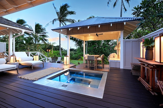 pool at dusk featuring ceiling fan, a deck, and an outdoor hot tub