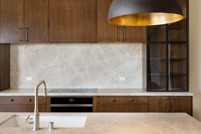 kitchen with backsplash, black cooktop, stainless steel oven, and sink