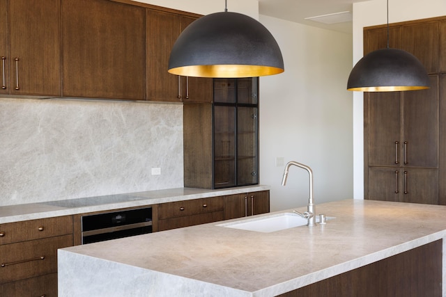 kitchen with stainless steel oven, backsplash, a kitchen island with sink, hanging light fixtures, and sink