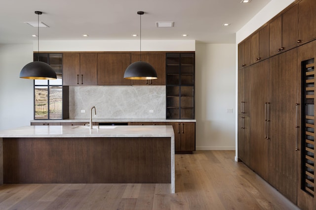 kitchen with decorative backsplash, light stone counters, sink, decorative light fixtures, and light hardwood / wood-style flooring