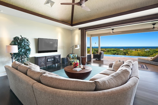 living room with ceiling fan, a raised ceiling, and dark wood-type flooring