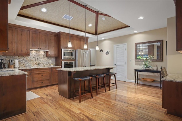 kitchen featuring light stone counters, a tray ceiling, stainless steel appliances, light hardwood / wood-style floors, and hanging light fixtures