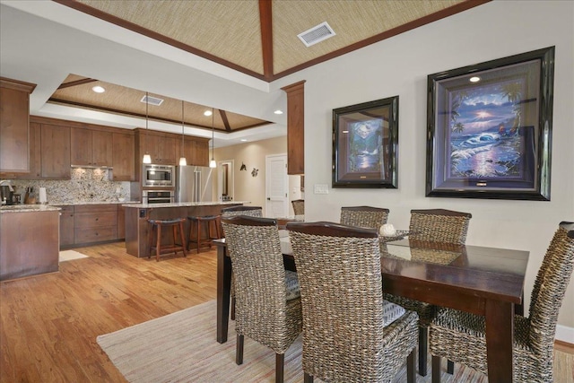 dining area featuring a raised ceiling, crown molding, and light hardwood / wood-style flooring