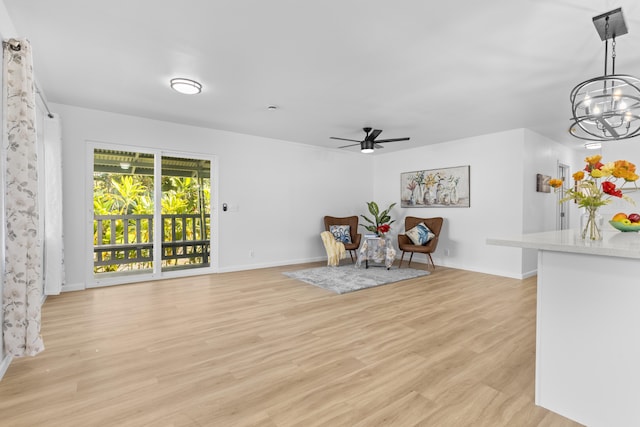 living area with ceiling fan with notable chandelier and light hardwood / wood-style floors