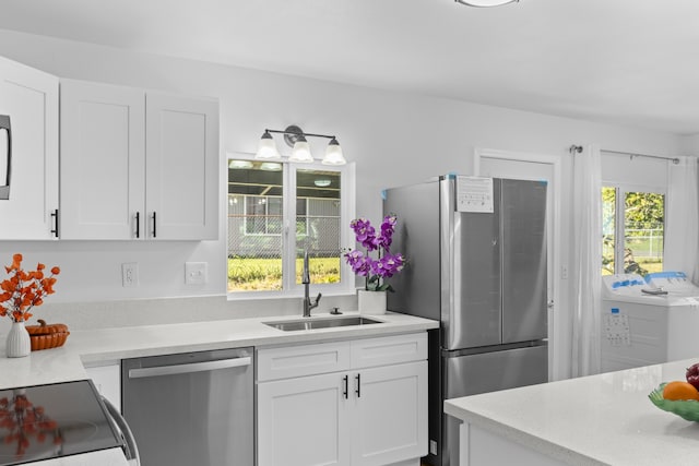 kitchen featuring sink, stainless steel appliances, washer / clothes dryer, plenty of natural light, and white cabinets