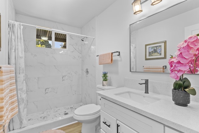 bathroom with hardwood / wood-style floors, vanity, toilet, and a tile shower