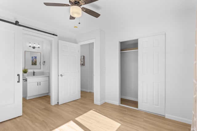 unfurnished bedroom featuring ceiling fan, a barn door, connected bathroom, and light hardwood / wood-style flooring