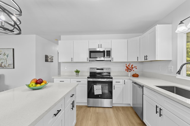 kitchen featuring stainless steel appliances, sink, an inviting chandelier, white cabinets, and light hardwood / wood-style floors