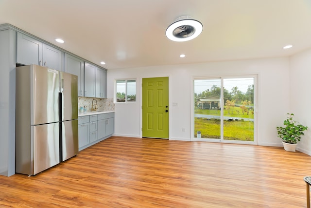 kitchen with gray cabinetry, sink, light hardwood / wood-style flooring, decorative backsplash, and stainless steel fridge