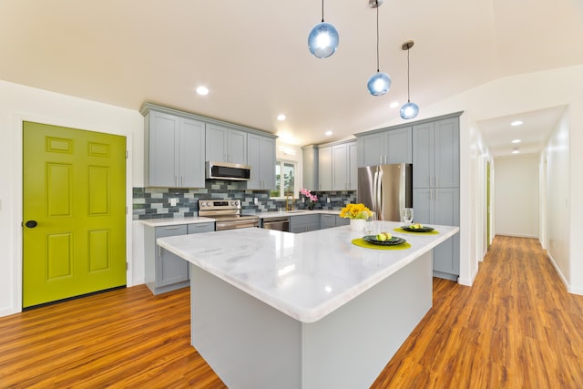 kitchen featuring a center island, hanging light fixtures, vaulted ceiling, light hardwood / wood-style flooring, and appliances with stainless steel finishes