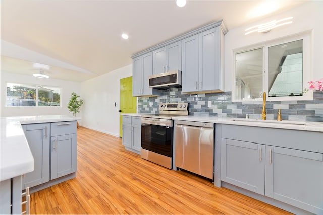 kitchen featuring gray cabinetry, backsplash, sink, light hardwood / wood-style floors, and stainless steel appliances