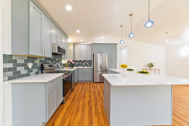 kitchen featuring pendant lighting, light hardwood / wood-style flooring, vaulted ceiling, decorative backsplash, and appliances with stainless steel finishes