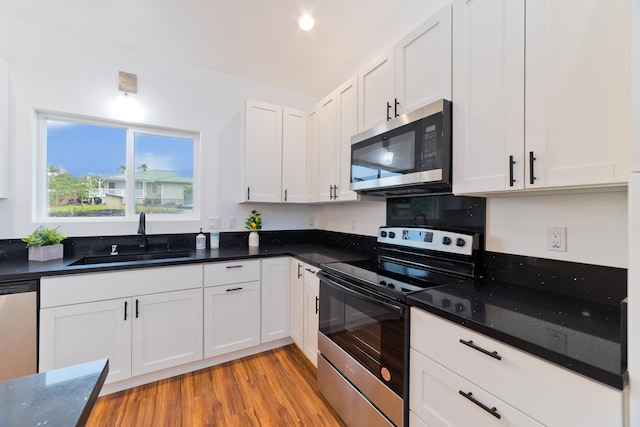 kitchen with appliances with stainless steel finishes, dark stone counters, sink, light hardwood / wood-style floors, and white cabinetry