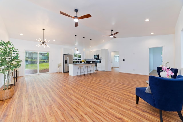 living room with ceiling fan with notable chandelier, vaulted ceiling, and light hardwood / wood-style flooring