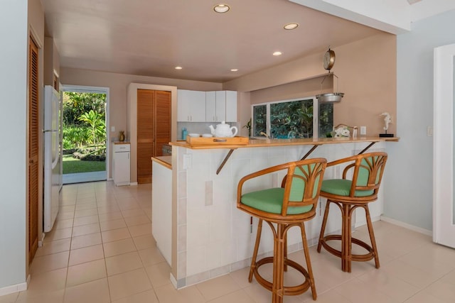 kitchen with kitchen peninsula, light tile patterned floors, white cabinets, white fridge, and a breakfast bar area