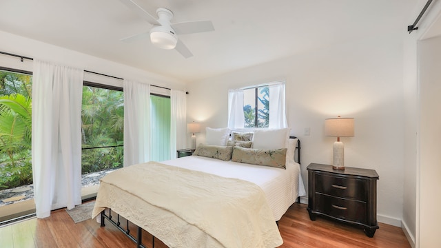 bedroom featuring ceiling fan, a barn door, wood-type flooring, and access to outside