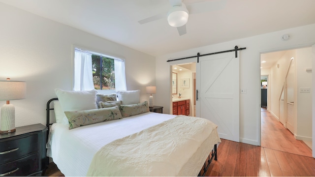 bedroom with hardwood / wood-style flooring, ceiling fan, a barn door, and connected bathroom