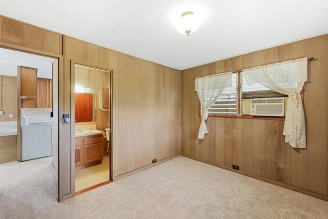 unfurnished bedroom featuring wooden walls, washer / dryer, sink, and light carpet