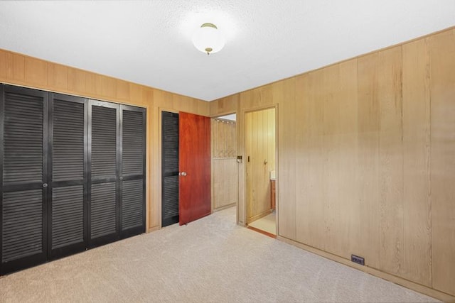 unfurnished bedroom featuring multiple closets, light carpet, and wooden walls