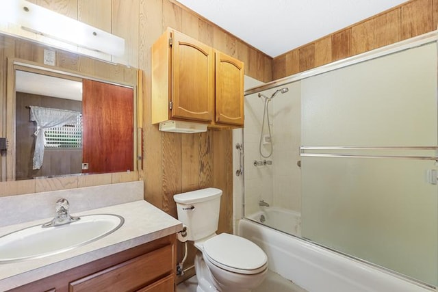 full bathroom with toilet, vanity, bath / shower combo with glass door, and wood walls