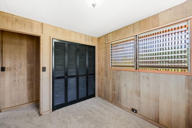 unfurnished bedroom featuring light colored carpet, wooden walls, a closet, and a textured ceiling