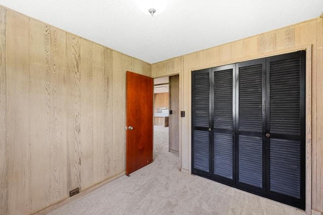 unfurnished bedroom with light colored carpet, a closet, and wood walls