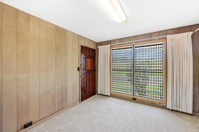 empty room featuring wooden walls, light carpet, and a textured ceiling