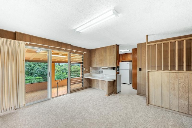 kitchen featuring wood walls, a textured ceiling, white refrigerator, kitchen peninsula, and light colored carpet