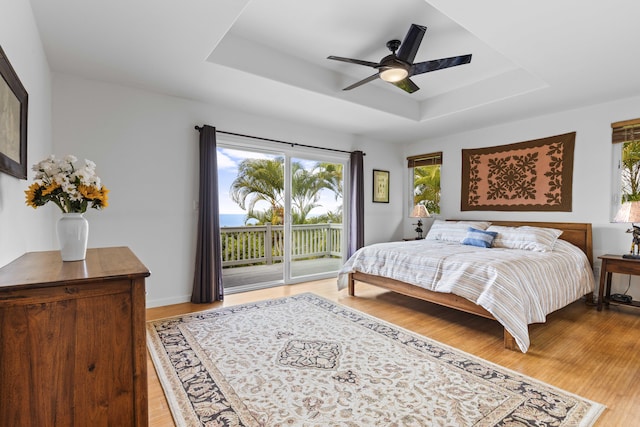 bedroom with wood-type flooring, access to exterior, ceiling fan, and a tray ceiling