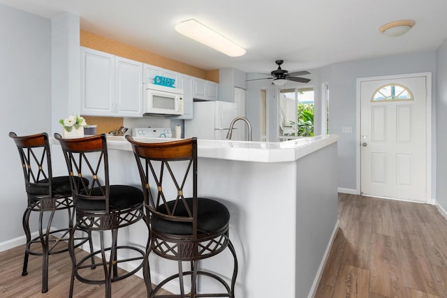 kitchen with ceiling fan, kitchen peninsula, white appliances, a breakfast bar, and white cabinets