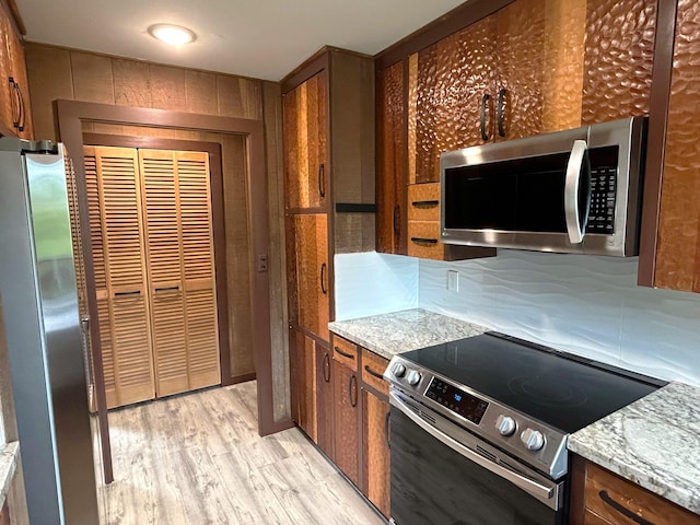 kitchen featuring light stone countertops, appliances with stainless steel finishes, and light hardwood / wood-style floors