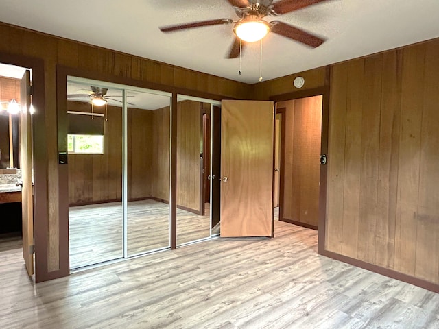 unfurnished bedroom featuring ceiling fan, two closets, light wood-type flooring, and wood walls