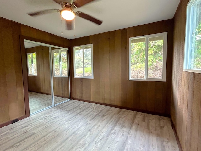 unfurnished bedroom featuring ceiling fan, wooden walls, light hardwood / wood-style floors, and a closet