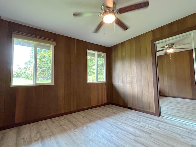 unfurnished bedroom featuring ceiling fan, wood walls, a closet, and light wood-type flooring