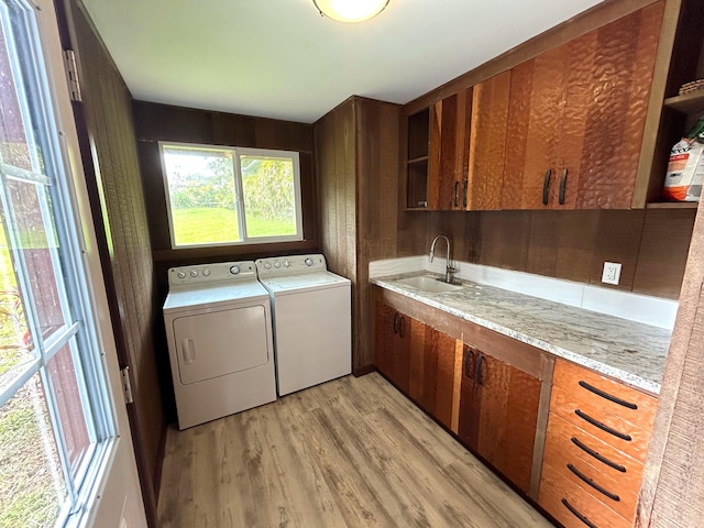 washroom with sink, wood walls, cabinets, separate washer and dryer, and light wood-type flooring