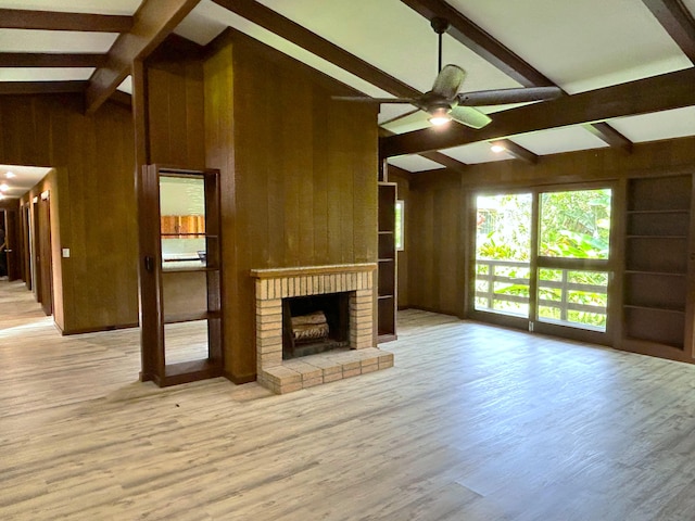 unfurnished living room with a brick fireplace, light wood-type flooring, lofted ceiling with beams, and wood walls