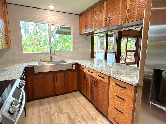 kitchen with sink, light hardwood / wood-style flooring, kitchen peninsula, stainless steel appliances, and light stone countertops