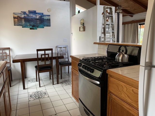 kitchen featuring black gas range oven, ceiling fan, tile countertops, wooden ceiling, and light tile patterned flooring