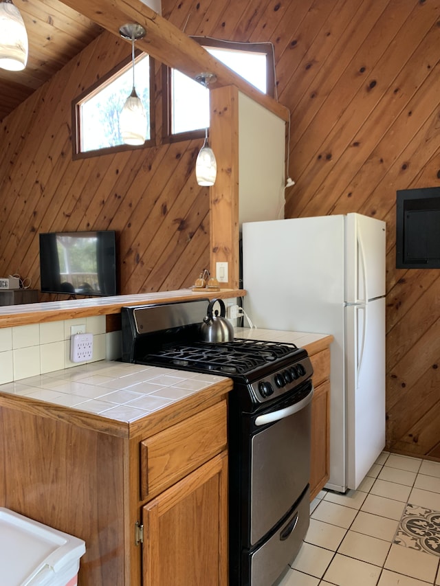 kitchen with gas range, wooden walls, pendant lighting, light tile patterned floors, and tile counters