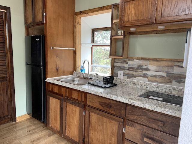 kitchen featuring light stone countertops, sink, tasteful backsplash, black fridge, and light hardwood / wood-style floors